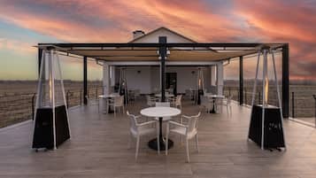 Un patio al aire libre con mesas y sillas, una zona cubierta y vistas al paisaje.