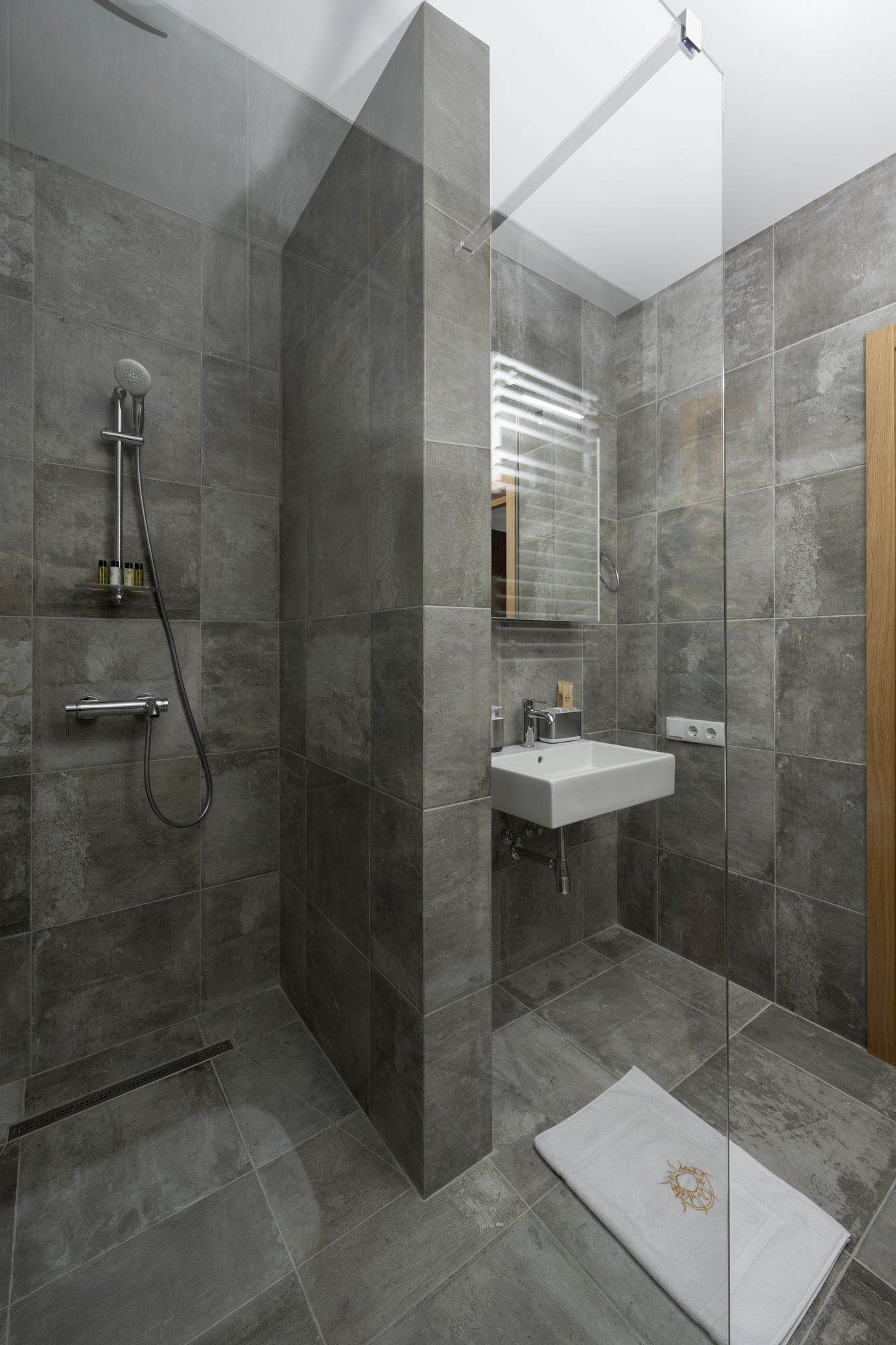 Une salle de bain moderne avec une douche à l’italienne en verre, un lavabo blanc et un grand miroir.