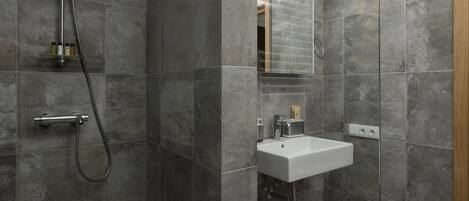 Une salle de bain moderne avec une douche à l’italienne en verre, un lavabo blanc et un grand miroir.