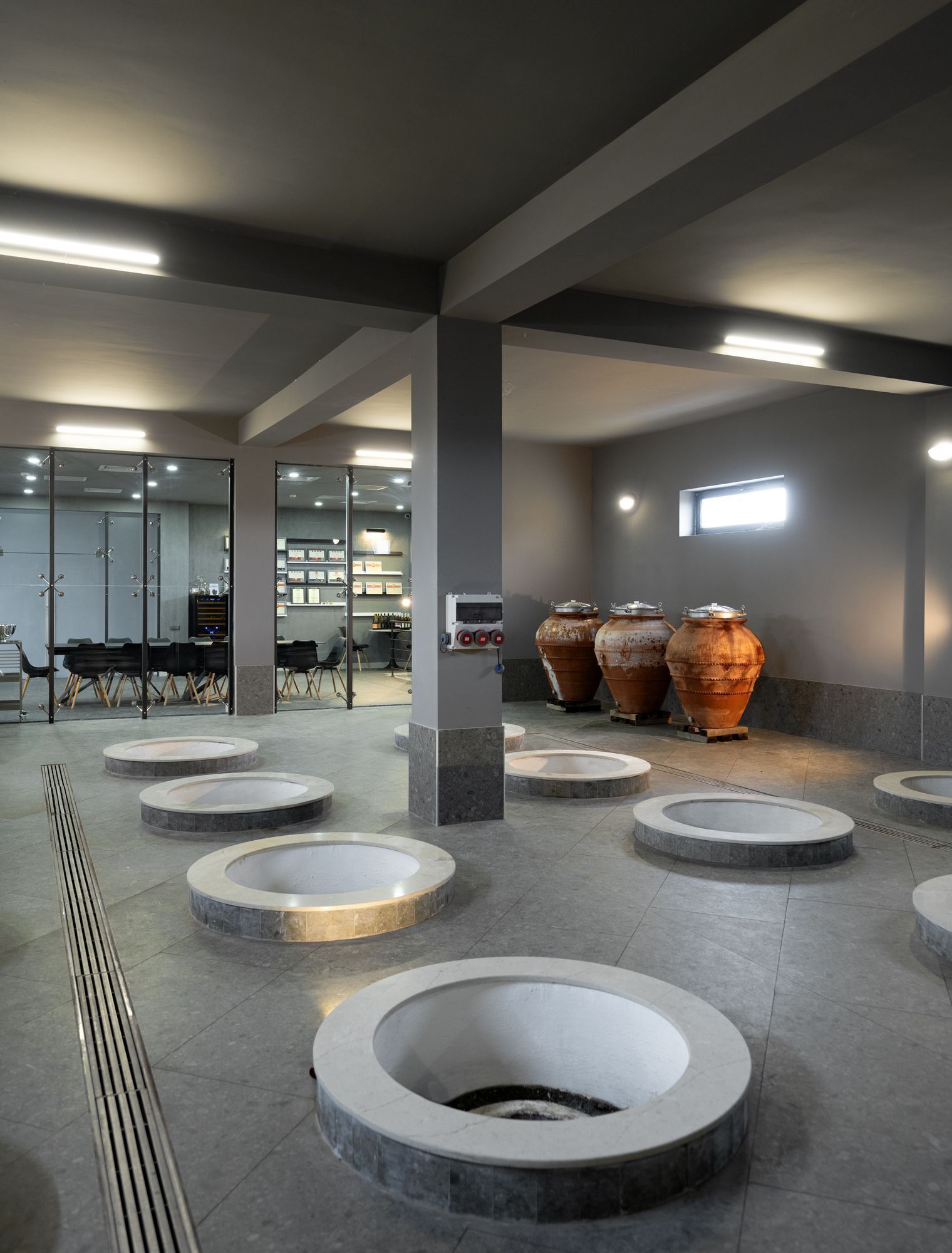 A modern indoor space with circular seating areas, large terracotta pots, and a visible ventilation system.