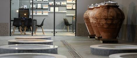 A modern interior with a glass wall displaying certificates, a large terracotta pot, and a seating area with a central table and chairs.