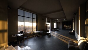 Een ruime kamer met grote ramen, een zithoek met banken en tafels, en uitzicht op een stadsbeeld.