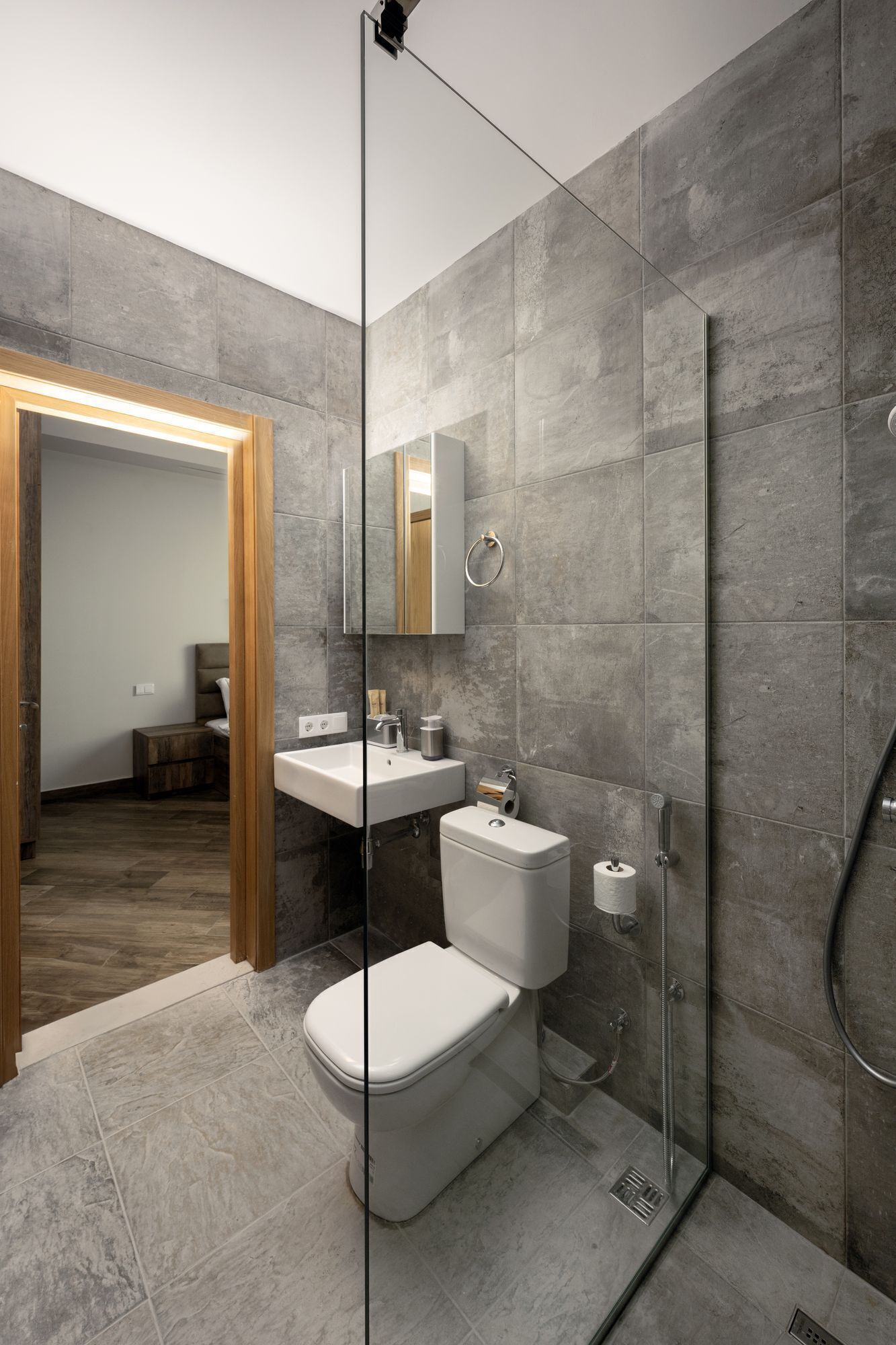 A modern bathroom with a glass shower enclosure, a white toilet, and a sink with a mirror above it.