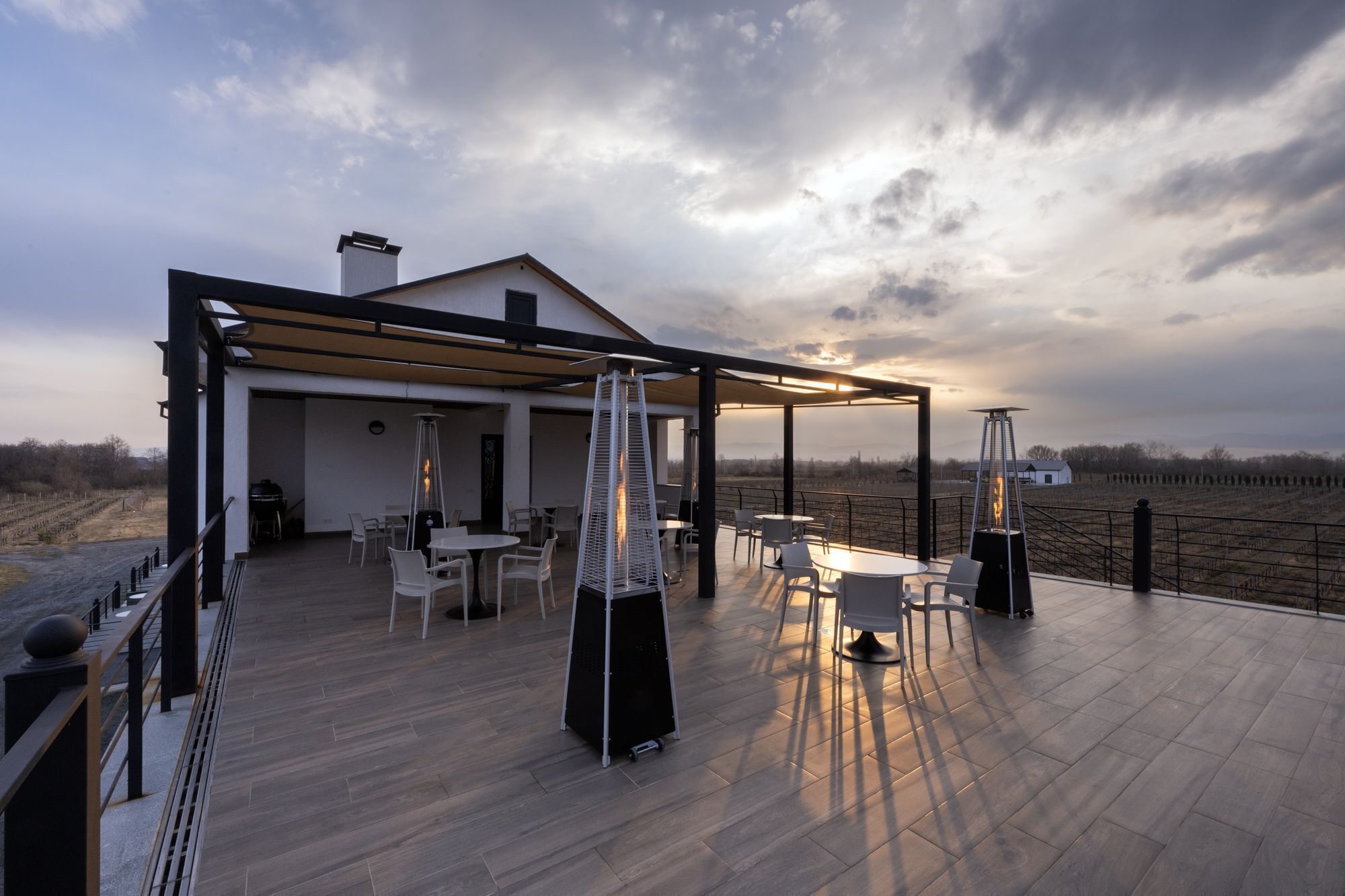 A modern outdoor patio with a pergola, seating, and a view of the vineyard.