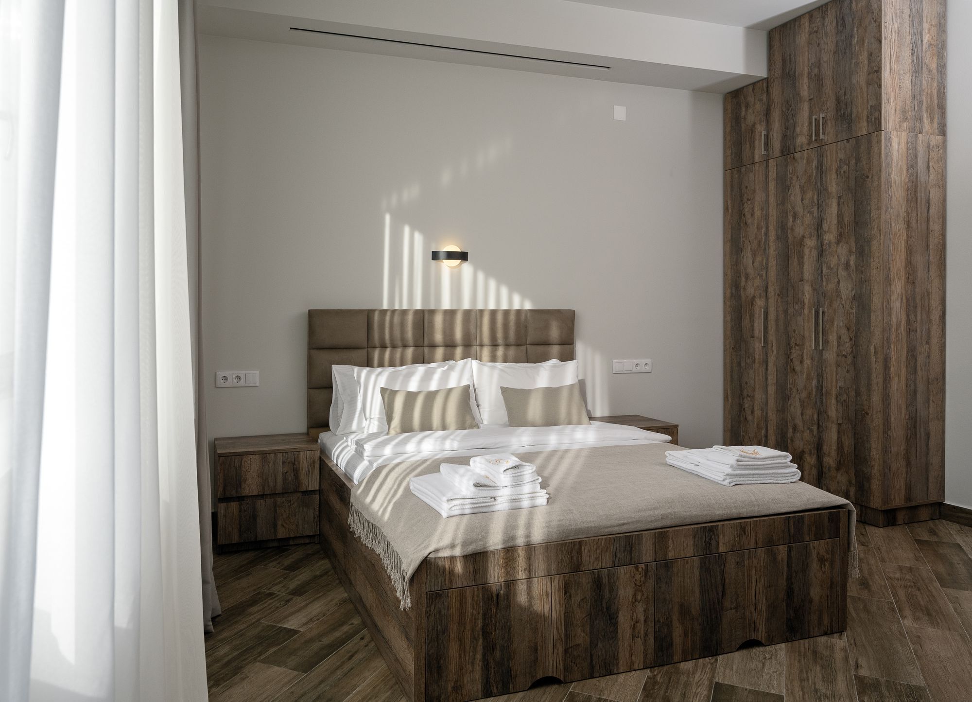 A modern bedroom with a wooden headboard, a bedside table, and a large wooden wardrobe.