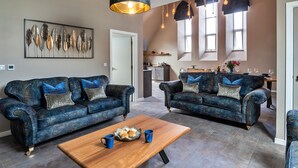 A spacious living room with two dark blue sofas, a wooden coffee table, and a large abstract art piece on the wall. - Chapel in Newquay Near Towan Beach (Newquay)