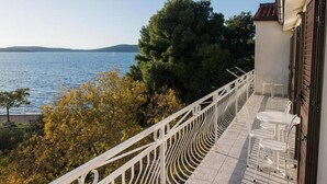 Ein Balkon mit weißer Brüstung, der auf ein Gewässer und Bäume blickt.
