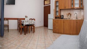Ein kompakter Wohnraum mit Esstisch, Stühlen, einer Küchenzeile, einer Couch und einem an der Wand befestigten Fernseher.