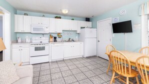 A compact kitchen with white cabinets, a microwave, stove, and refrigerator. There is a wooden dining table with chairs and a small sofa.