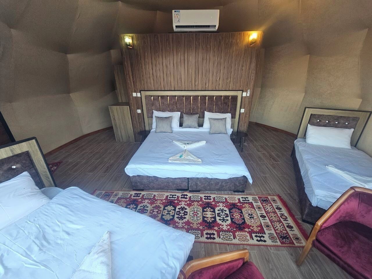 Una camera d'albergo con due letti, un tappeto a motivi decorativi e una testata del letto in legno.