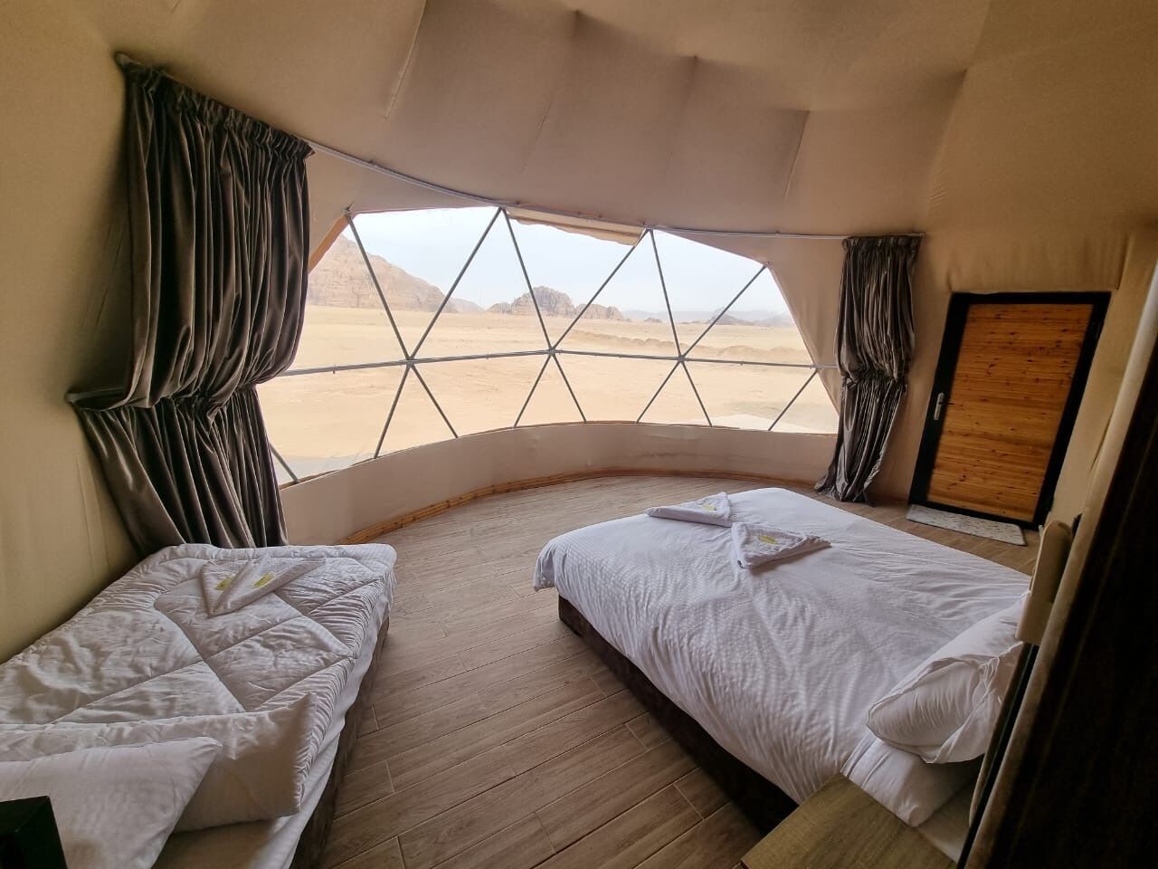 A room with two beds, a large window, and a view of a desert landscape.