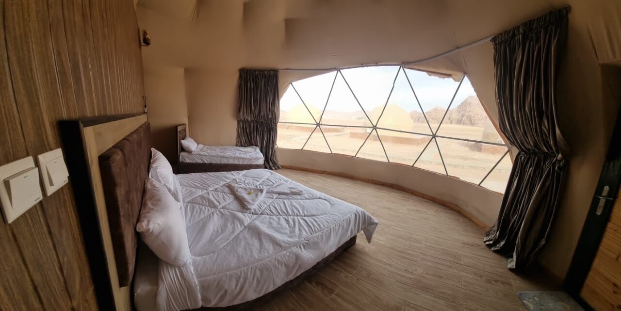 A bedroom with two beds, a large window, and a view of the desert.