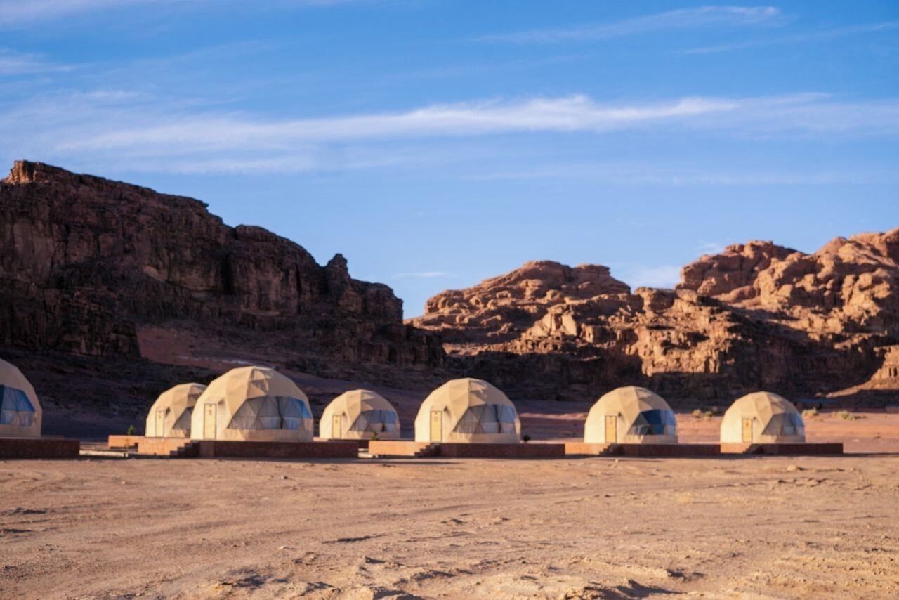 A row of dome-shaped tents in a desert setting with rocky cliffs in the background.