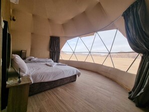 Un dormitorio con un amplio ventanal que ofrece vista al desierto, una cama con ropa blanca y suelo de madera.