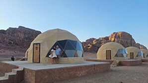 A desert landscape with multiple dome-shaped tents, each with a door and a small set of steps leading up to the entrance. - Wadi Rum Desert Camp (Wadi Rum)