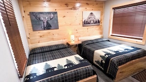 A room with two beds, a bench, wooden walls, and ceiling lights. - Escape to the tranquility of our cozy cabin inn, where rustic charm meets modern comfort. Experience a home away from home ambiance. (Spencerport)