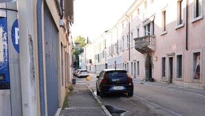 Een smalle straat met gebouwen, een geparkeerde auto en een blauw bord aan de linkerkant.