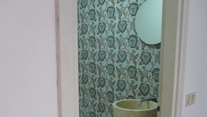 Een badkamer met behang met een patroon, een groot wastafel en een rode kruk.