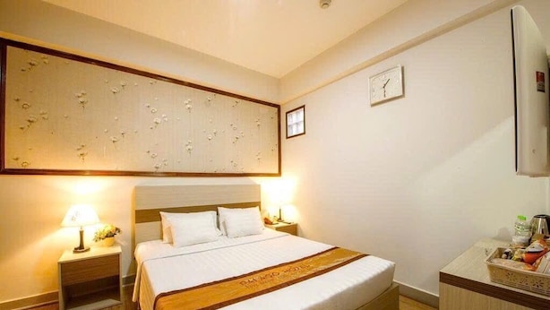 Une chambre d’hôtel avec un grand lit, deux tables de chevet avec des lampes, une tête de lit en bois, une horloge murale et un mini-bar.