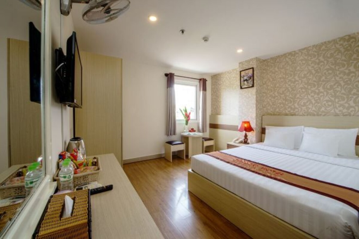 A hotel room with a bed, a desk with a lamp, a TV, and a window with curtains.