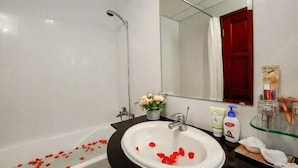 Une salle de bain avec un lavabo blanc, un miroir, une douche et des articles de toilette posés sur le comptoir.
