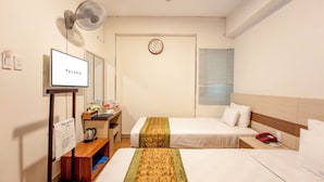 Une chambre d’hôtel avec deux lits, une télévision, un bureau avec une machine à café, un ventilateur et une horloge murale.