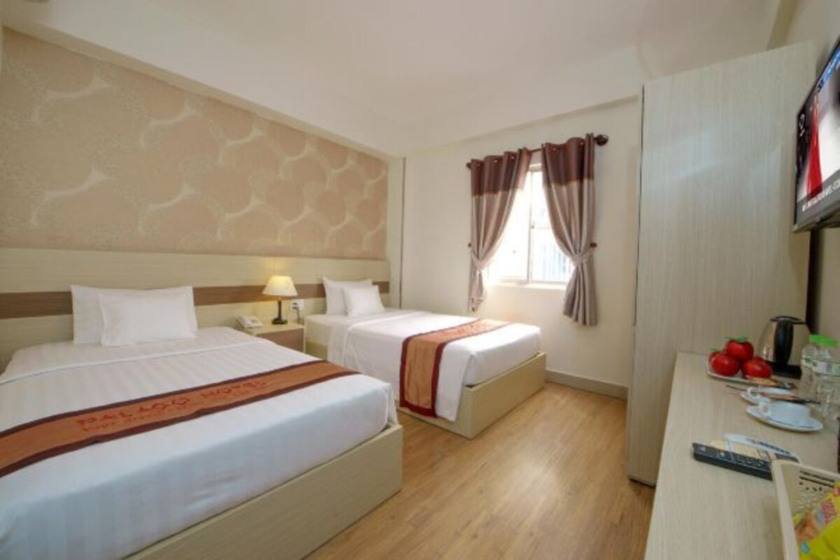 A hotel room with two beds, a desk with a TV, and a window with curtains.