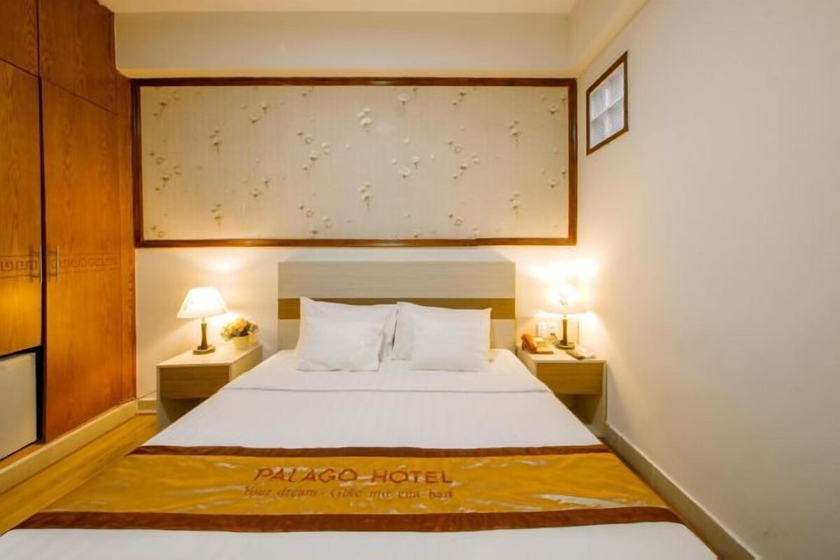 Une chambre d’hôtel avec un grand lit, deux tables de chevet avec des lampes, une armoire en bois et un panneau décoratif mural.