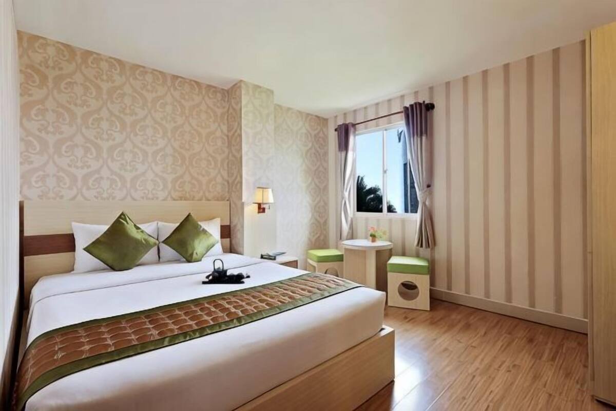 Ein Hotelzimmer mit einem großen Bett, Nachttischen, einem Fenster mit Vorhängen und einer Wand mit Muster.