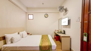 Une chambre d’hôtel avec un lit, un bureau, une télévision et une horloge au mur.