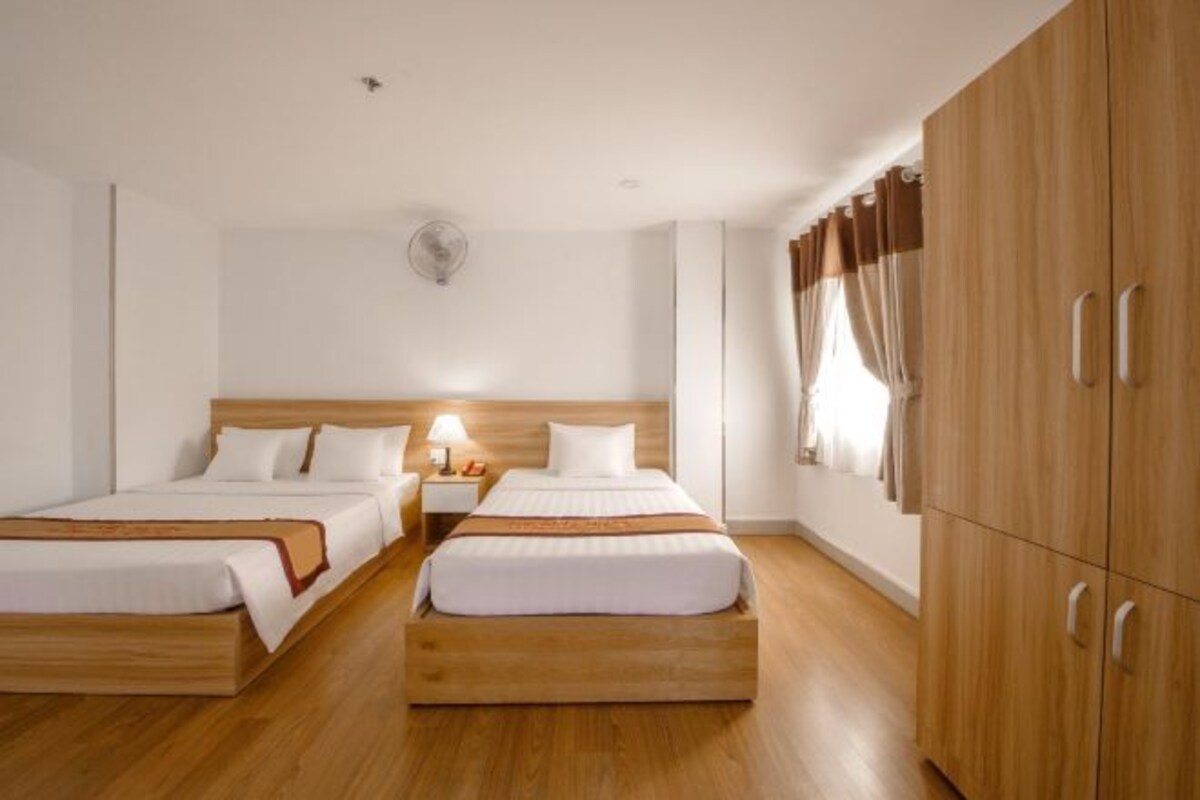 A double room with two beds, wooden headboards, a bedside table with a lamp, a wardrobe, and a ceiling fan.