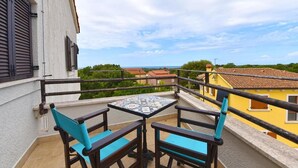 Un balcón con dos sillas y una mesa pequeña, con vistas a una zona residencial con casas y vegetación.