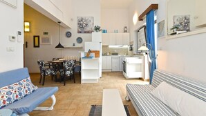 Un espacio habitable compacto con kitchenette, comedor y zona de estar con sofá y banca.
