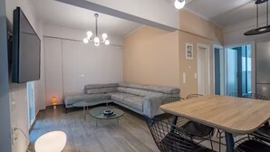 Una sala de estar moderna con un sofá modular, una mesa de comedor con sillas, un televisor de pantalla plana montado en la pared y una lámpara colgante.
