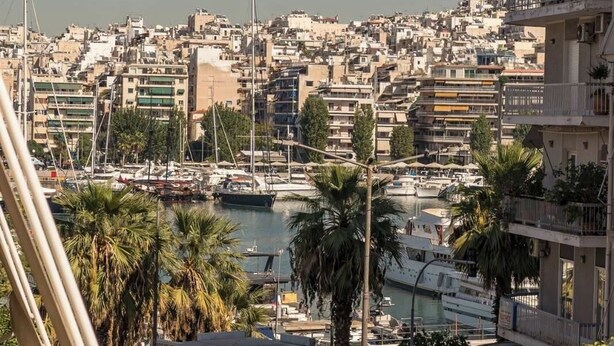 Un paisaje urbano costero con edificios densos, un puerto deportivo con barcos y un edificio destacado con balcones.