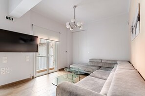 A modern living room with a flat-screen TV, a glass coffee table, and a grey sectional sofa. - Luxury Serenity-Cozy Stay by the Sea and Marina (Pireas)