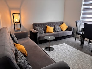 A modern living room with a grey sofa, a small round table, and a patterned rug.