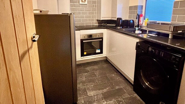 Eine kleine Küche mit Kühlschrank, Backofen, Geschirrspüler und einer Wandverkleidung aus Ziegelsteinen.