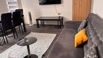 A living room with a grey sofa, a black table, and a TV mounted on the wall.