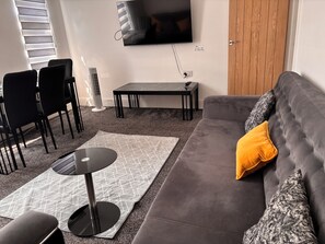 A living room with a grey sofa, a black table, and a TV mounted on the wall.