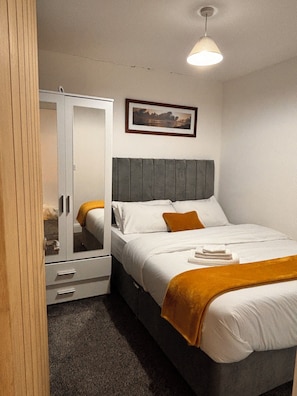 A bedroom with a bed, a wardrobe, a framed picture on the wall, and a ceiling light.