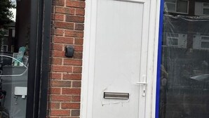 Une porte blanche avec une fente pour le courrier, un mur de briques et une porte vitrée dotée d’un cadre bleu.
