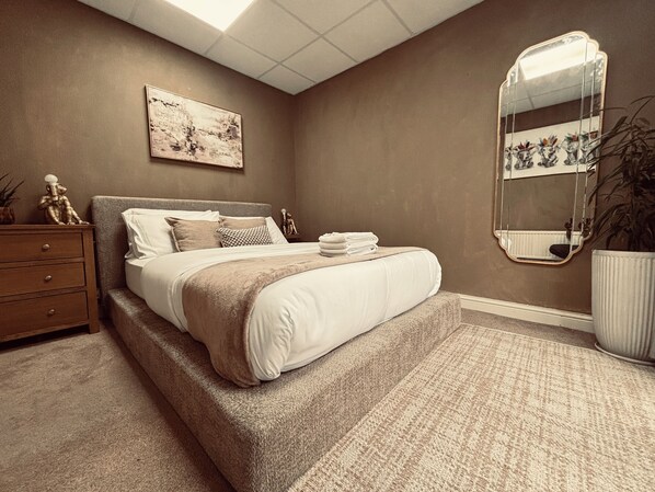 A bedroom with a bed, a nightstand, a mirror, and a painting on the wall.