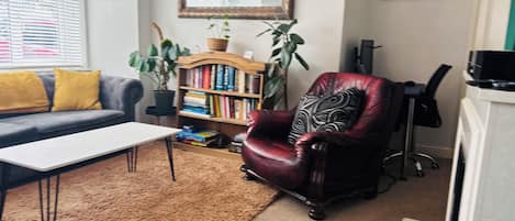 A living room with a sofa, a coffee table, a bookshelf, a red armchair, a mirror, and a potted plant.