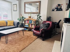 A living room with a sofa, a coffee table, a bookshelf, a red armchair, a mirror, and a potted plant.