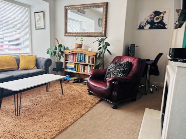 A living room with a sofa, a coffee table, a bookshelf, a red armchair, a mirror, and a potted plant.
