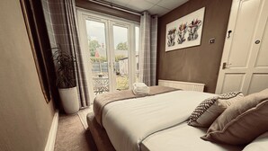 A hotel room with a large bed, a view through a sliding door, a potted plant, and a painting on the wall.