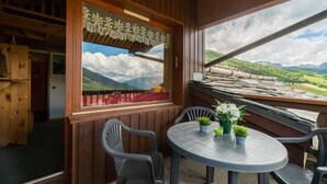 En træhytte med balkon, et rundt bord med stole og udsigt til grønne bakker.