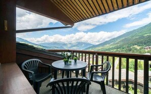 Ein Balkon mit Bergblick, einem runden Tisch mit Stühlen und einer kleinen Blumenkomposition.