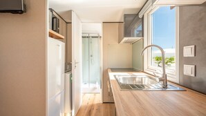 A modern kitchen with a built-in oven, a sink, and a window overlooking a garden.
